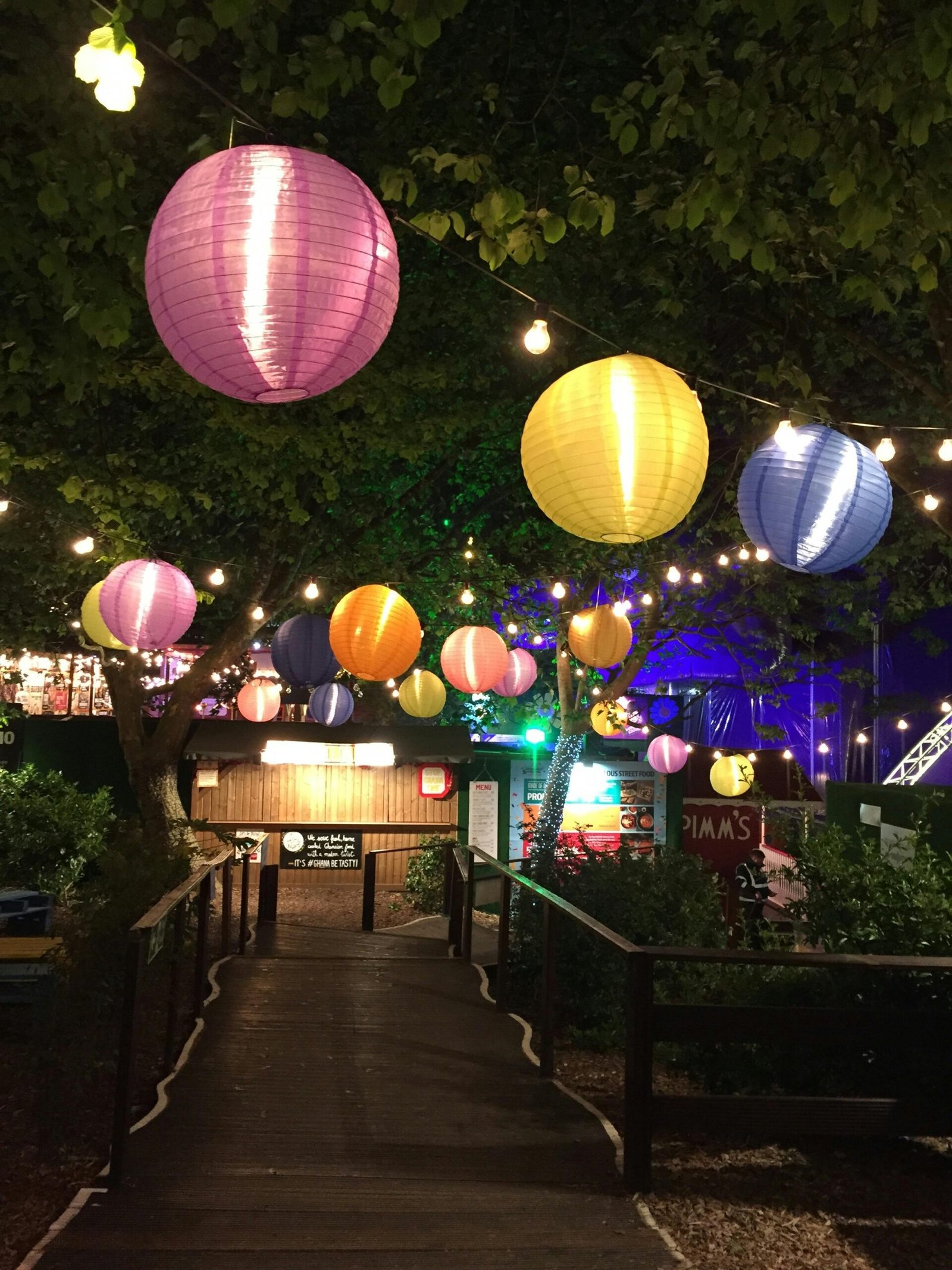 Vibrant paper lanterns hanging over a garden path during a festive night celebration outdoors.